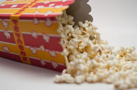 Popcorn spilling from red and yellow movie-theatre-style box, on a white background